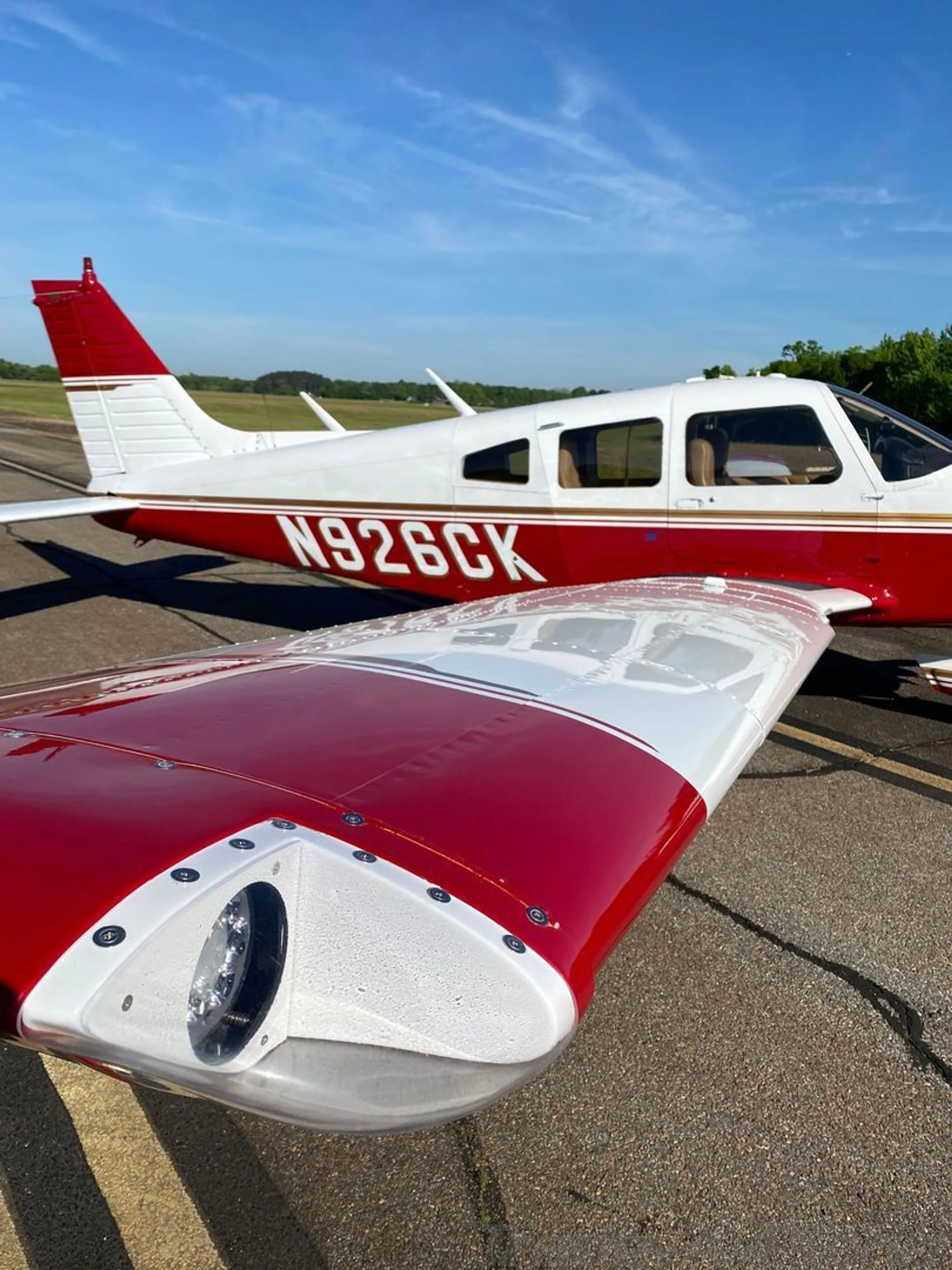 A close-up view of the left wingtip and fuselage of a white and red Piper Arrow II (N926CK) on the tarmac.