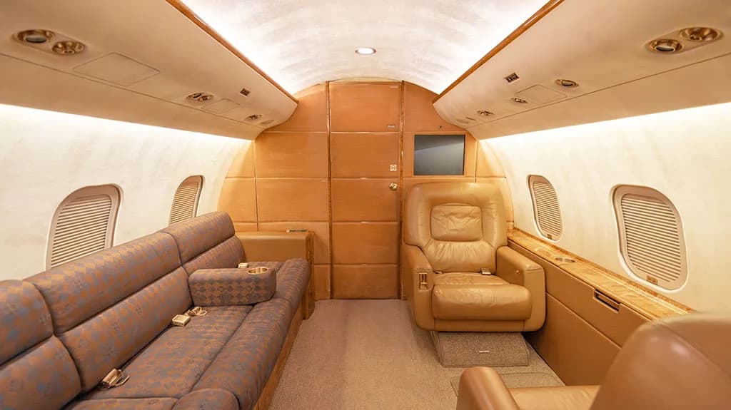 A section of the private jet cabin with a patterned sofa and a single tan leather armchair.