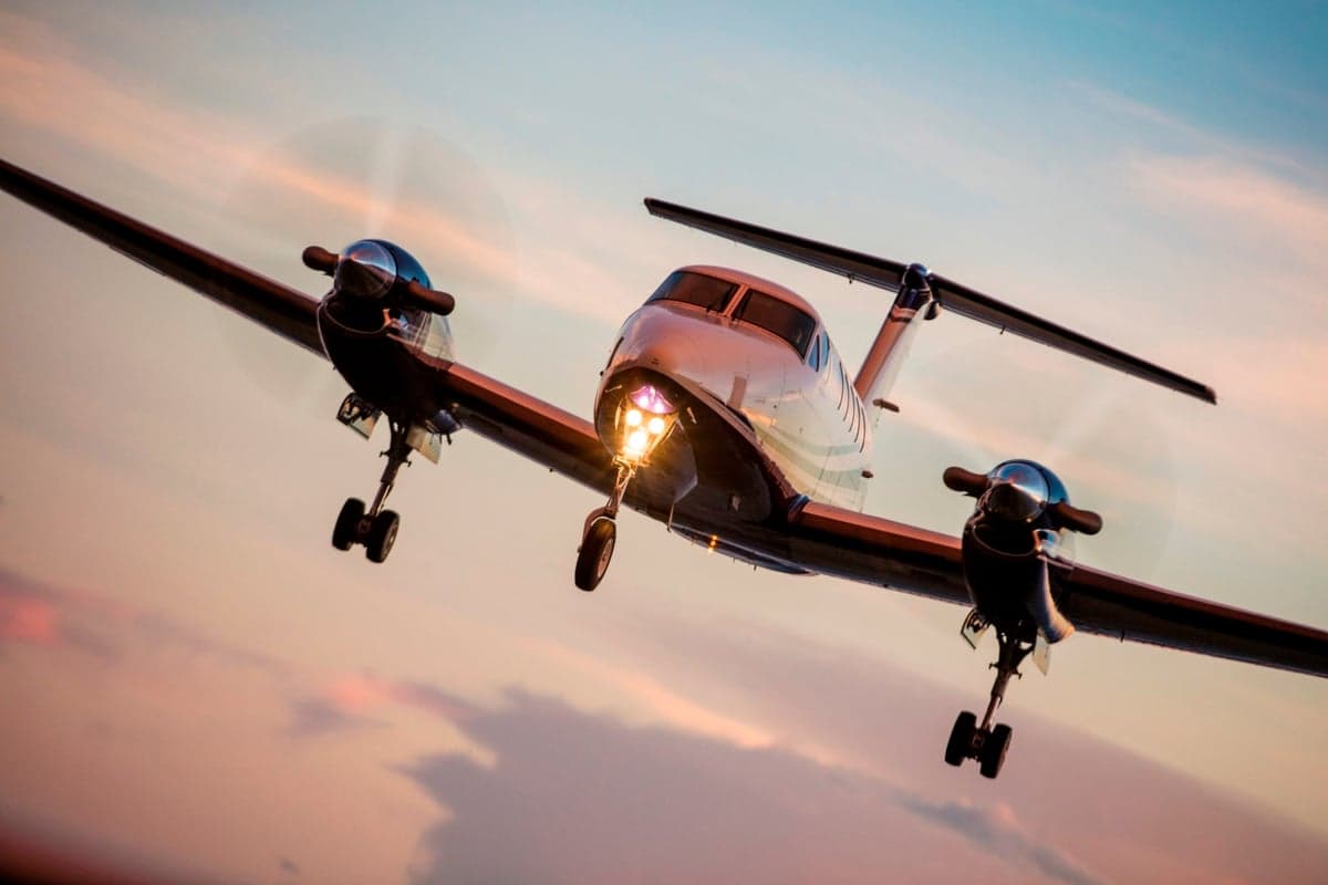 A white and black King Air 350i with landing gear extended approaches against a colorful sunset sky.