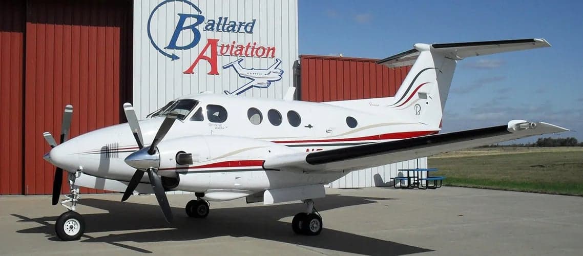 Beechcraft King Air with a white and red paint scheme parked in front of a hangar.