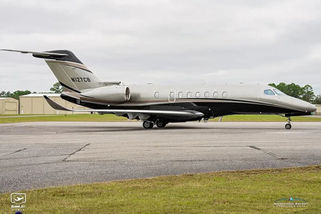 A side view of a grey and black business jet with registration N127CB on a tarmac under a cloudy sky.