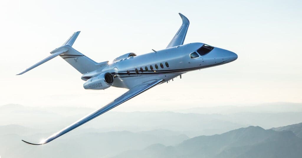 A Citation Longitude jet in flight over a mountainous landscape.