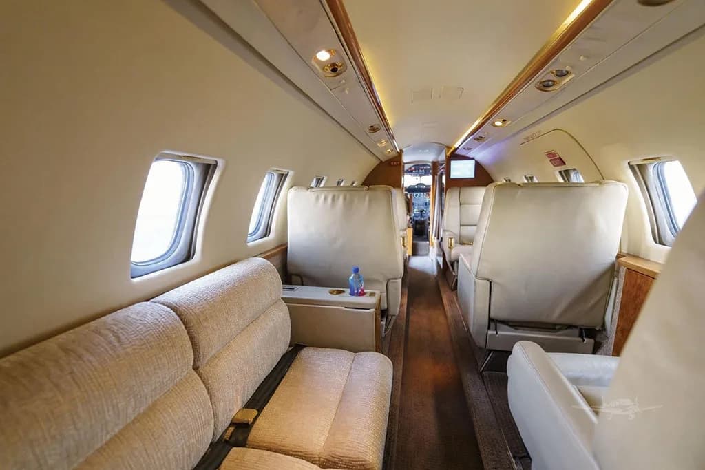 A wide view of the Dassault Falcon 50's cabin, showing a beige fabric divan on the left and beige leather club seats extending towards the cockpit.