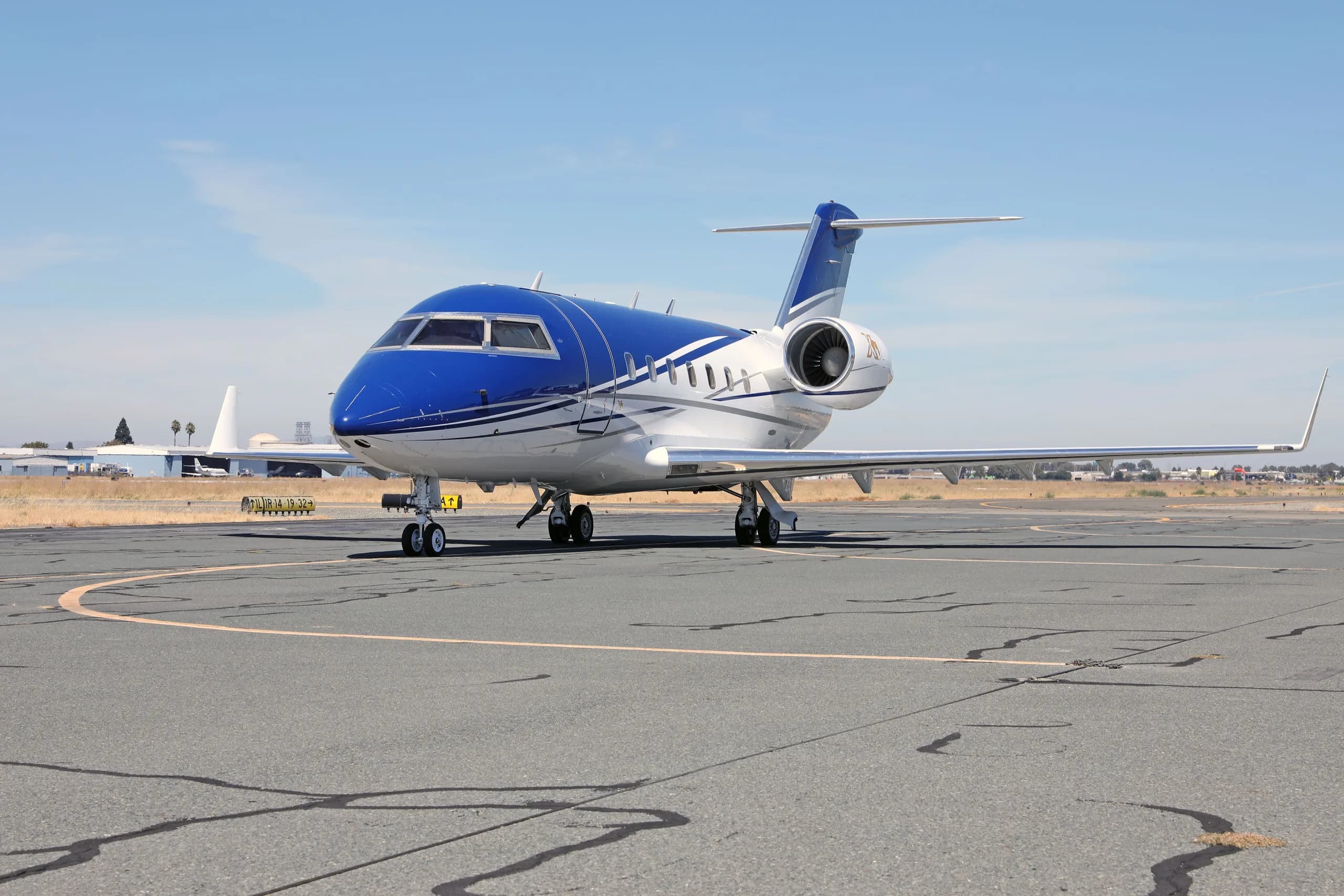 A blue and white Bombardier Challenger 604 aircraft (N436DM) parked on a tarmac, viewed from the front-left.