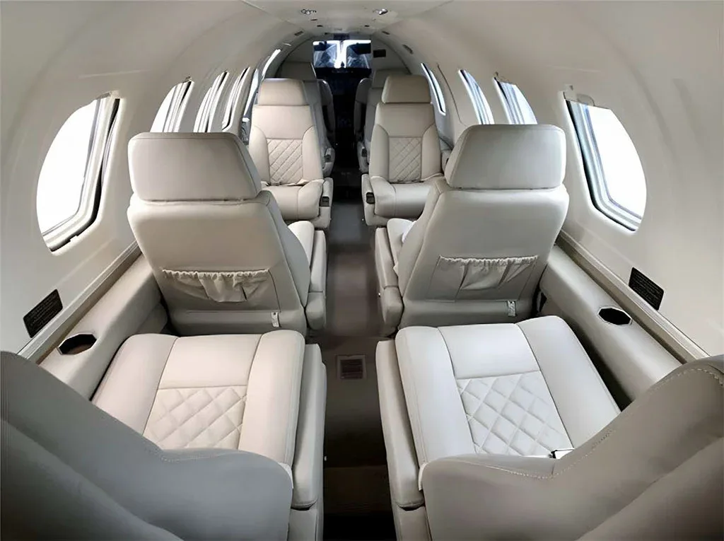 The spacious cabin interior of a business jet, featuring light-colored leather seats with quilted stitching, viewed from the rear.
