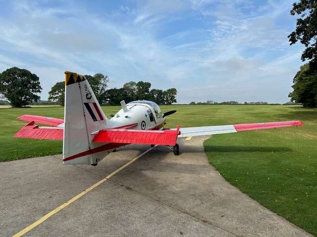 A red and white Bulldog aircraft parked on a paved area with a grassy field in the background.