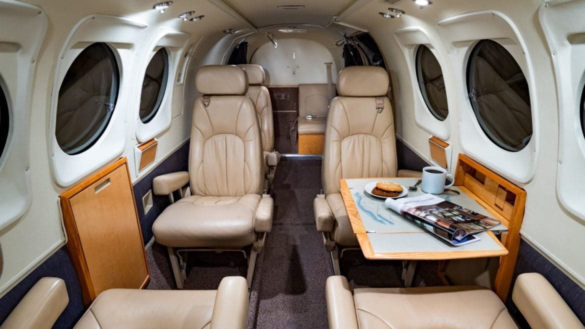 Spacious aircraft cabin featuring leather seating and a table with refreshments.