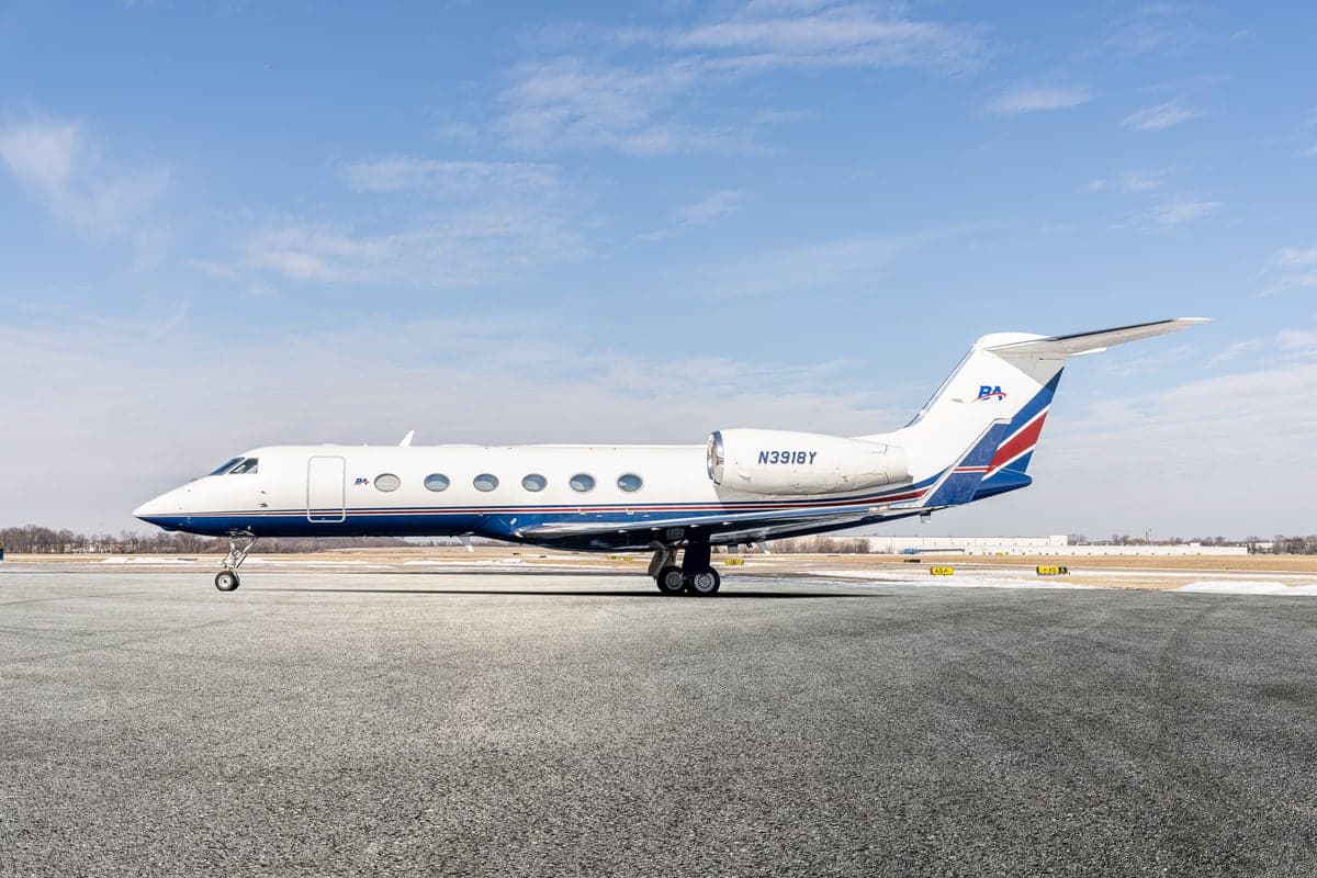 A Gulfstream G-IV aircraft is parked on the tarmac with a blue and red stripe paint scheme.