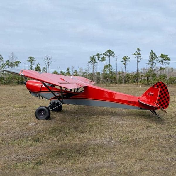 A red and gray Legend Cub aircraft is parked on a grassy field.