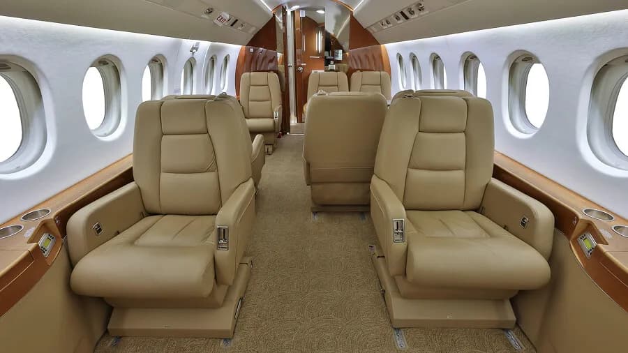 The luxurious tan leather interior cabin of a business jet with multiple passenger seats.