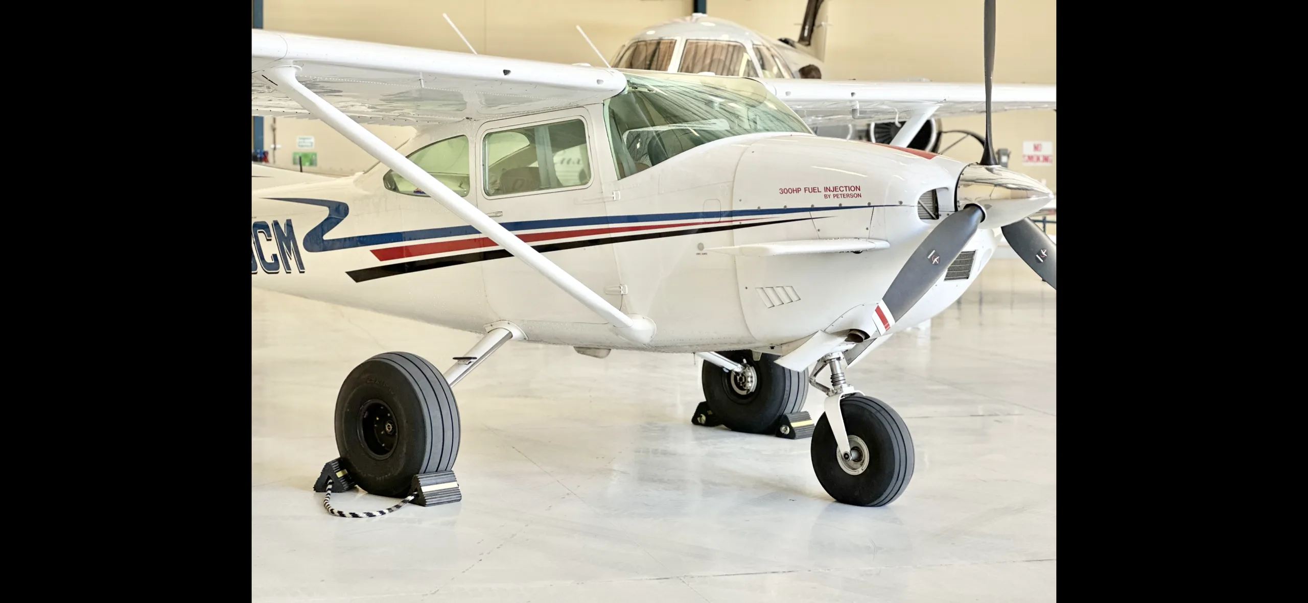 A white single-engine propeller aircraft with red and blue stripes on the fuselage, parked inside a hangar.