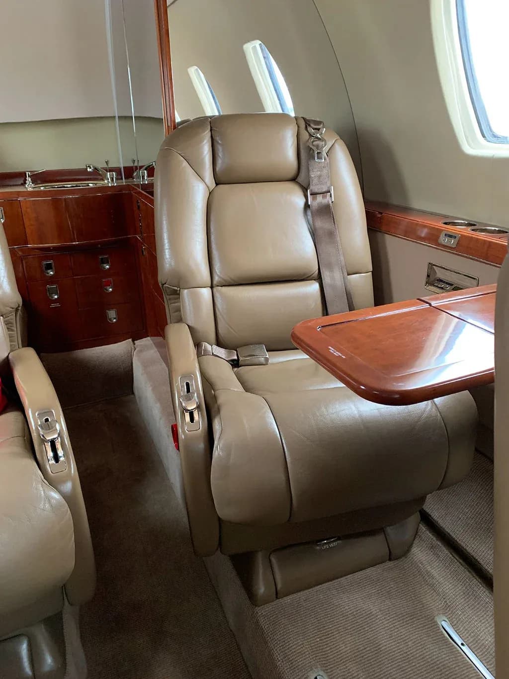 A tan leather seat with a fold-out table in the aircraft cabin.