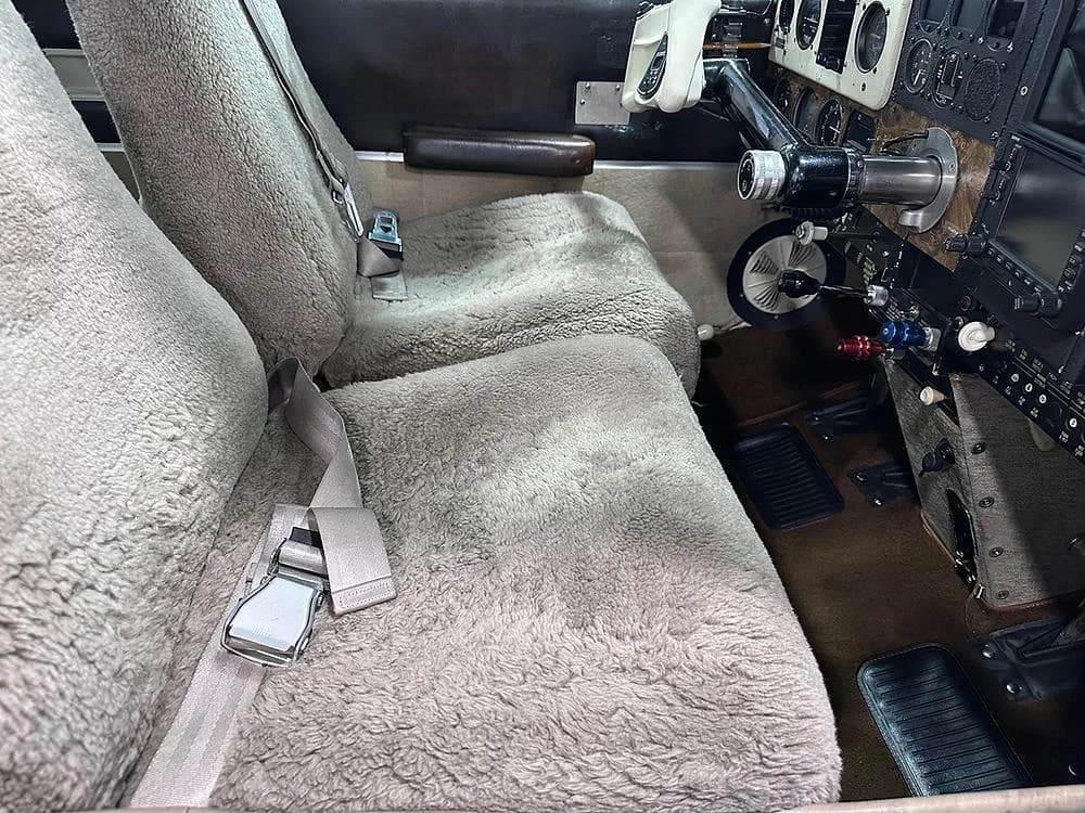 Interior view of an aircraft cabin with two front seats covered in light brown sheepskin.