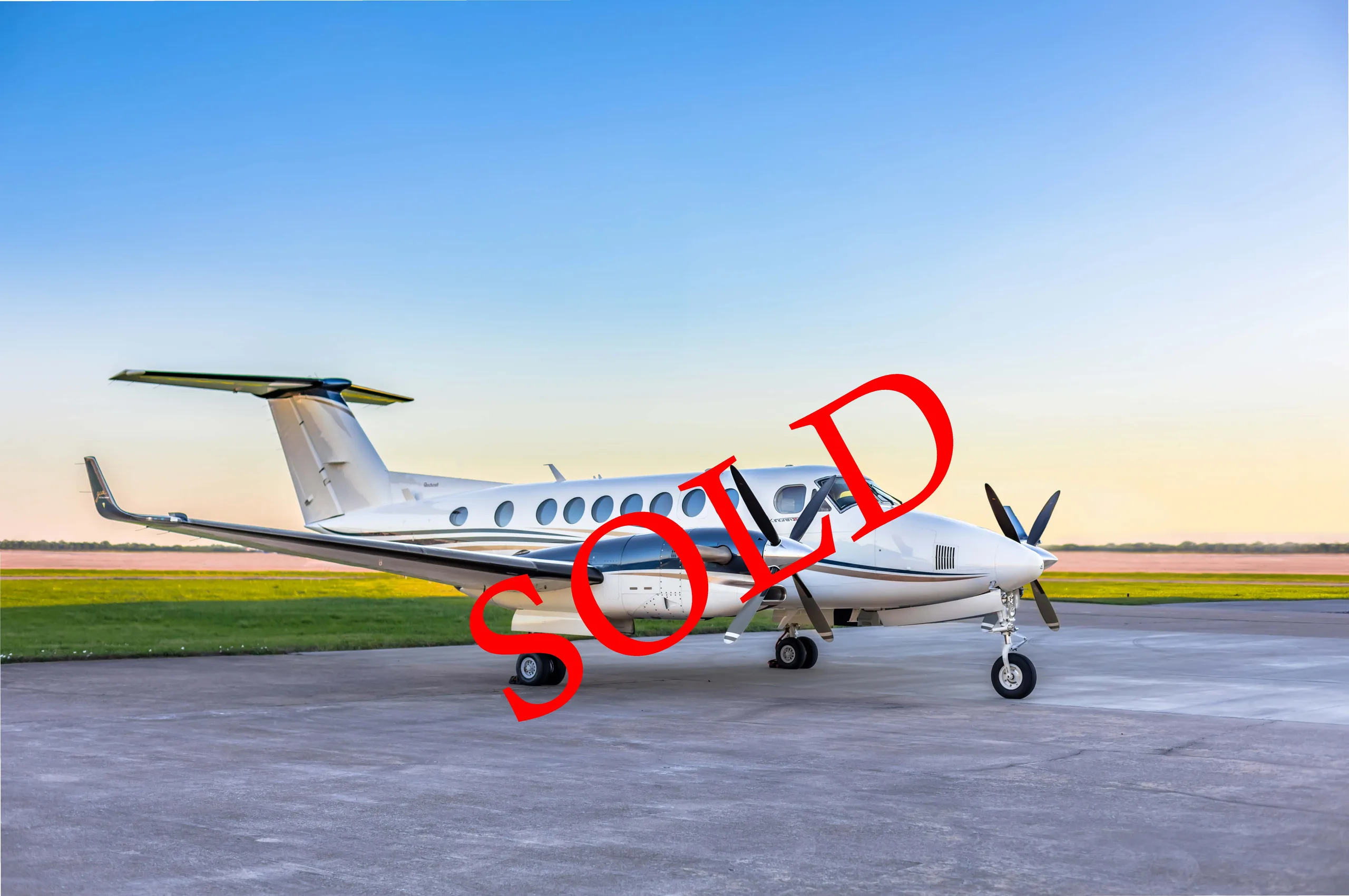 A white and black Beechcraft King Air 350i turboprop aircraft with "SOLD" text, parked on an airfield at sunset.
