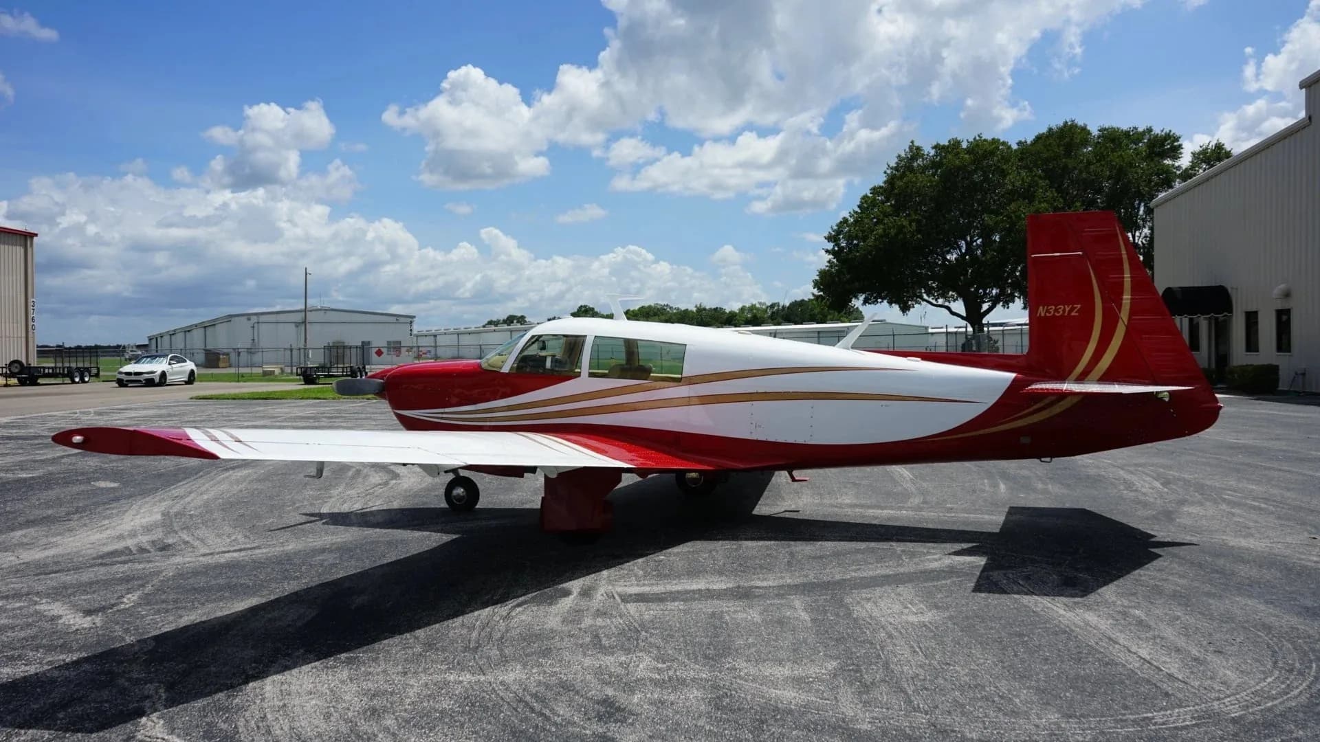 A full side view of the red and white single-engine aircraft, N33YZ, parked on an asphalt apron.