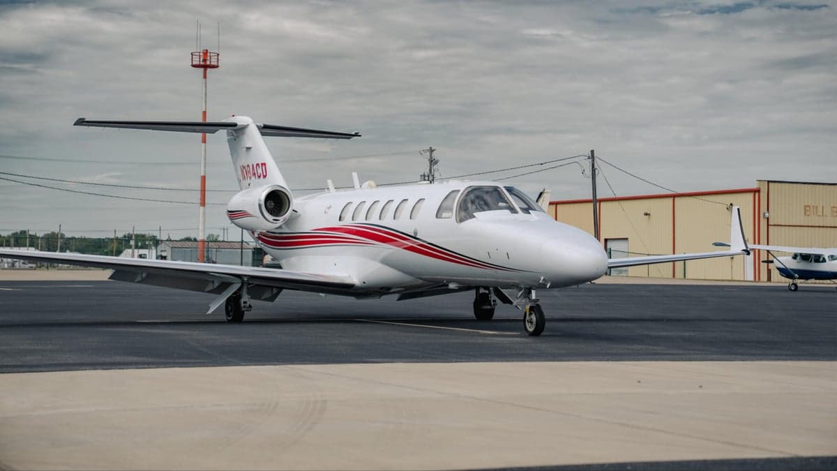 A white Citation CJ2 aircraft with red stripes is parked on the tarmac.