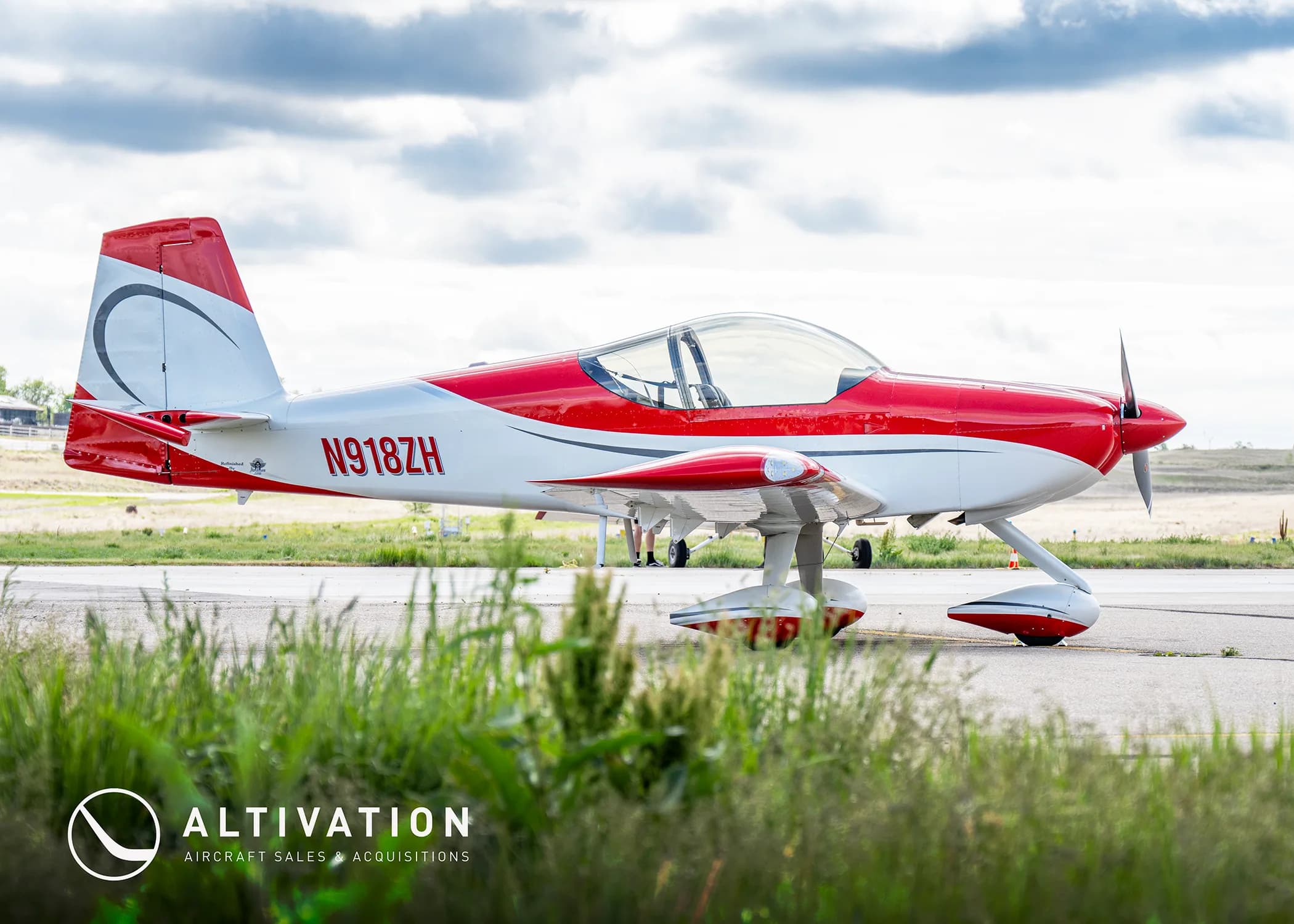 A red and white experimental aircraft with registration N918ZH parked on an airfield, viewed from the side with grass in the foreground.