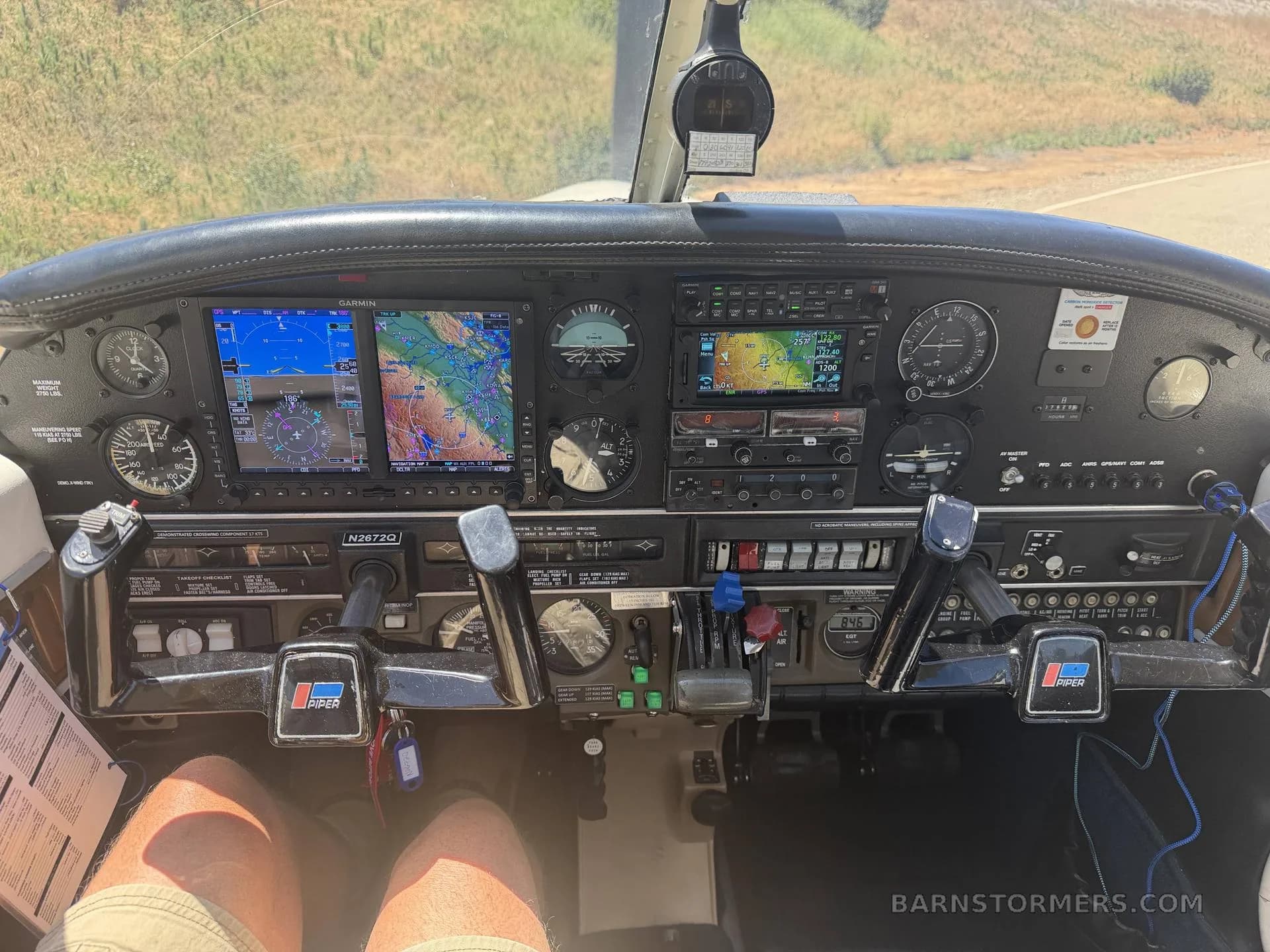 The cockpit of a Piper Arrow III, showing the instrument panel with multiple Garmin displays and dual yokes.