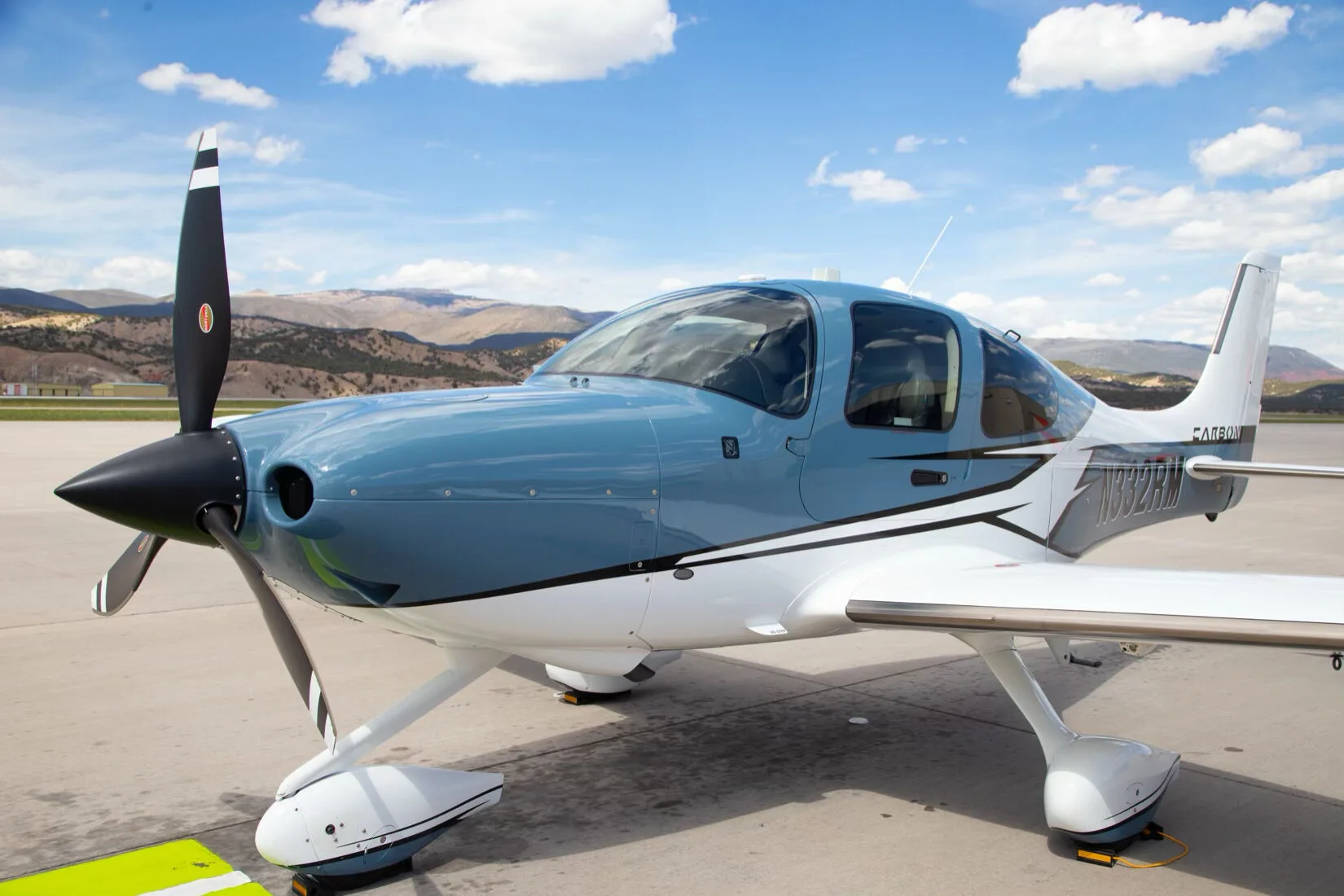 Close-up front-side view of a blue and white Cirrus SR22T GTS aircraft, registration N332RM, parked on an airport tarmac.