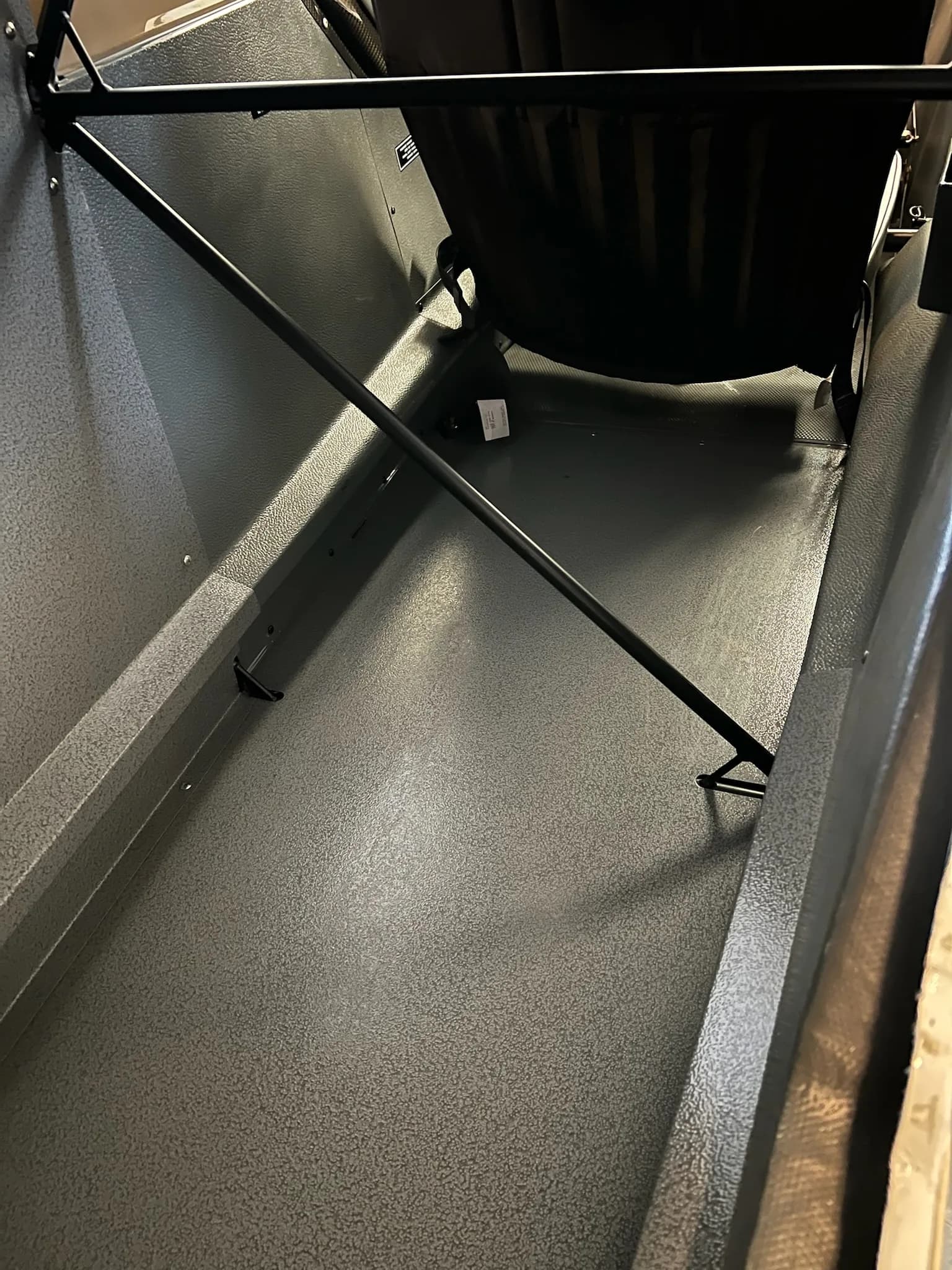The gray-textured cargo area or rear storage compartment of an aircraft, showing internal structural bars.