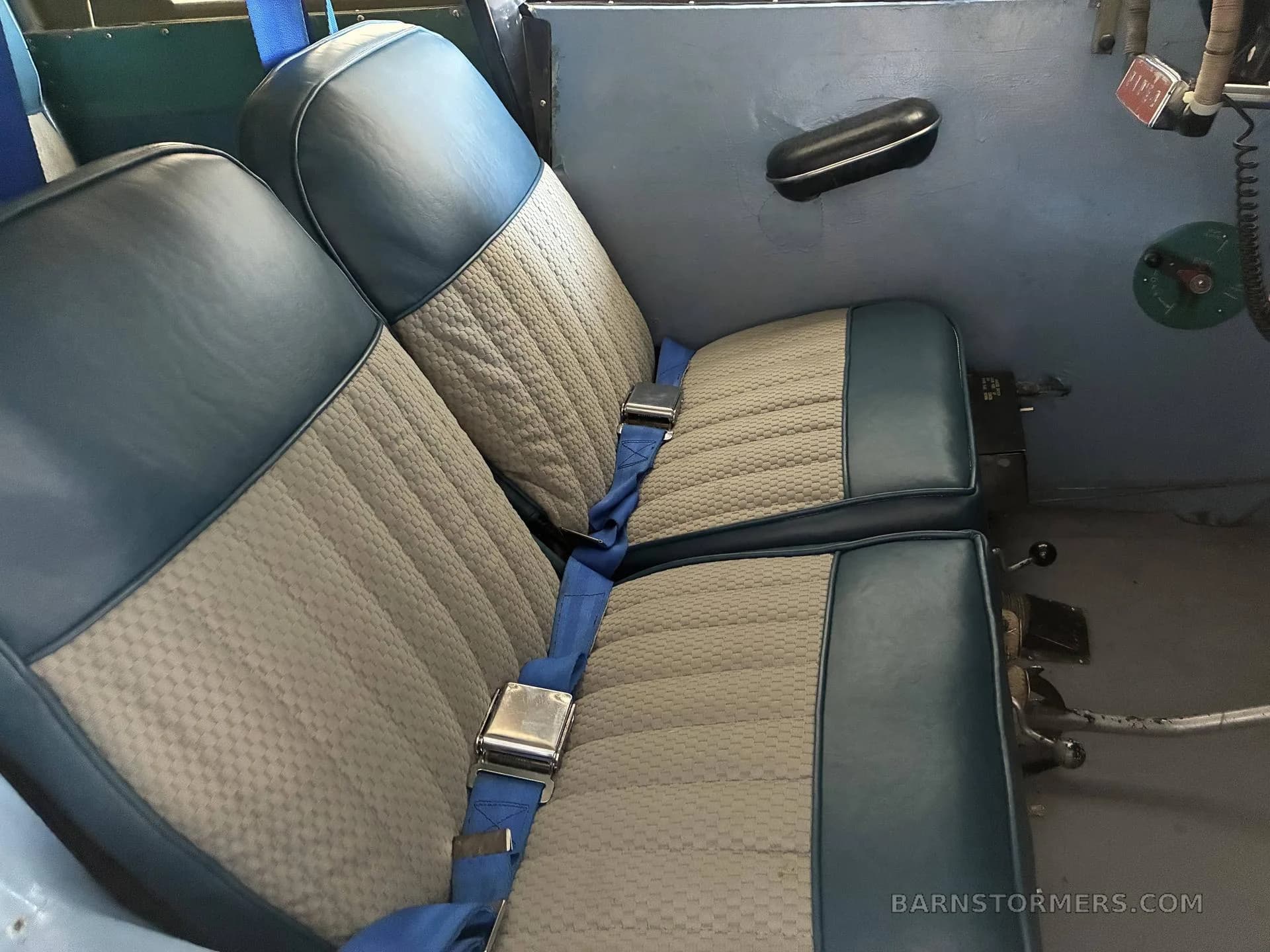 Two aircraft seats with blue leather and light gray fabric upholstery, featuring blue seatbelts.