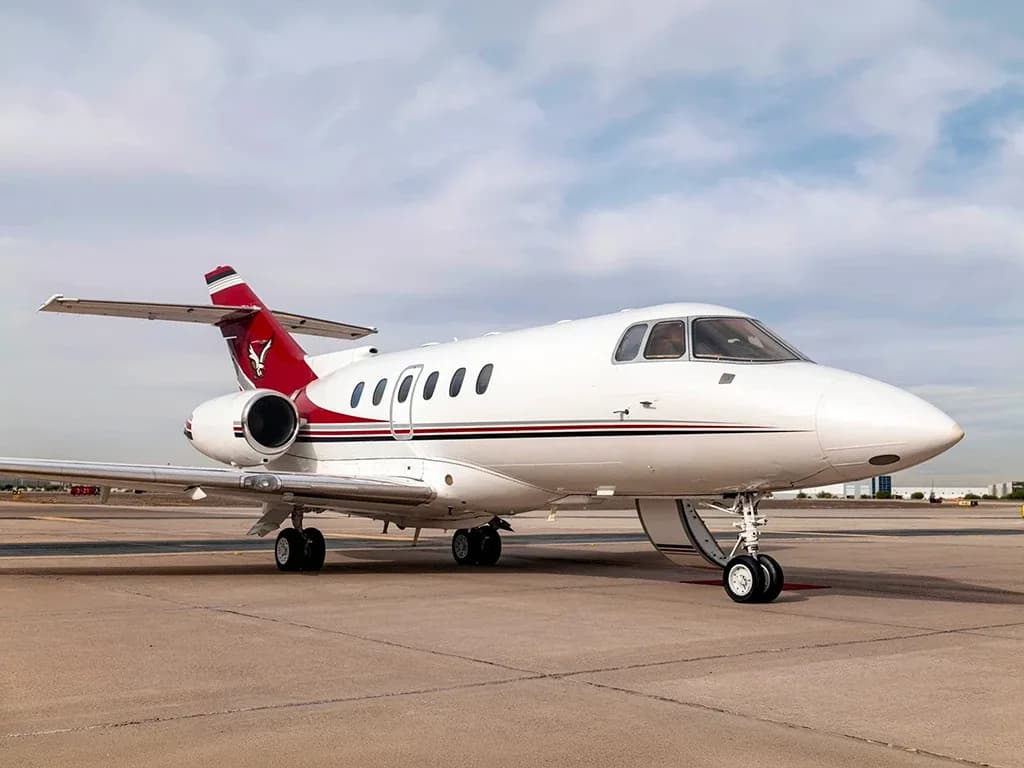 A white business jet with a red tail featuring a bull logo and red and black stripes, parked on an airport tarmac.