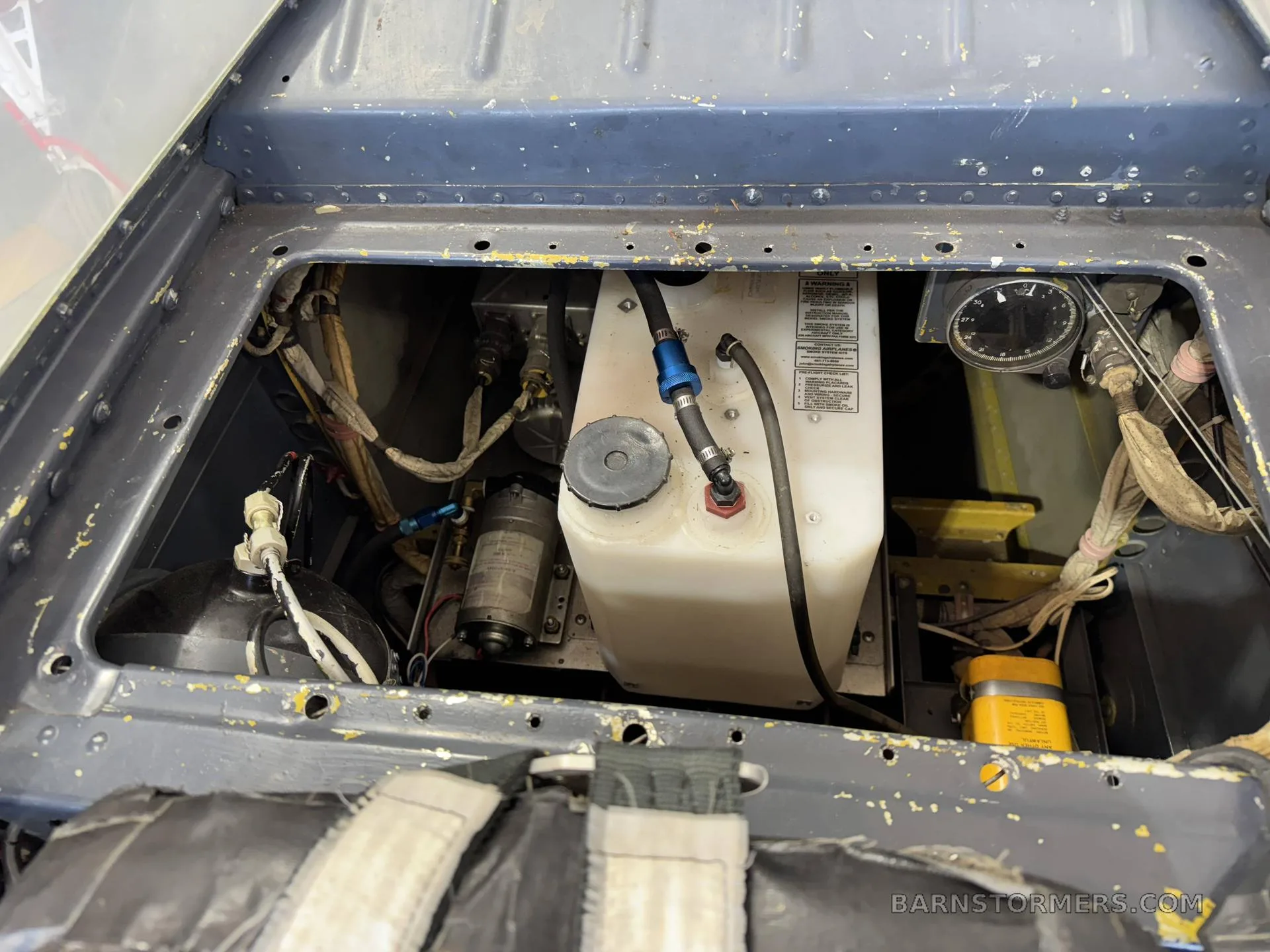 An open compartment revealing internal aircraft components, including a white fluid reservoir, pumps, and wiring.
