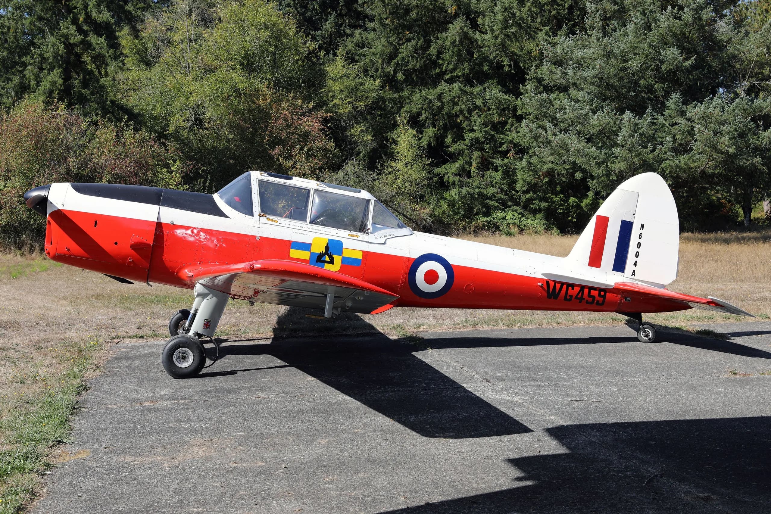 A red, white, and black de Havilland Canada DHC-1 Chipmunk aircraft with British roundels and "WC459" markings, parked on an airfield.