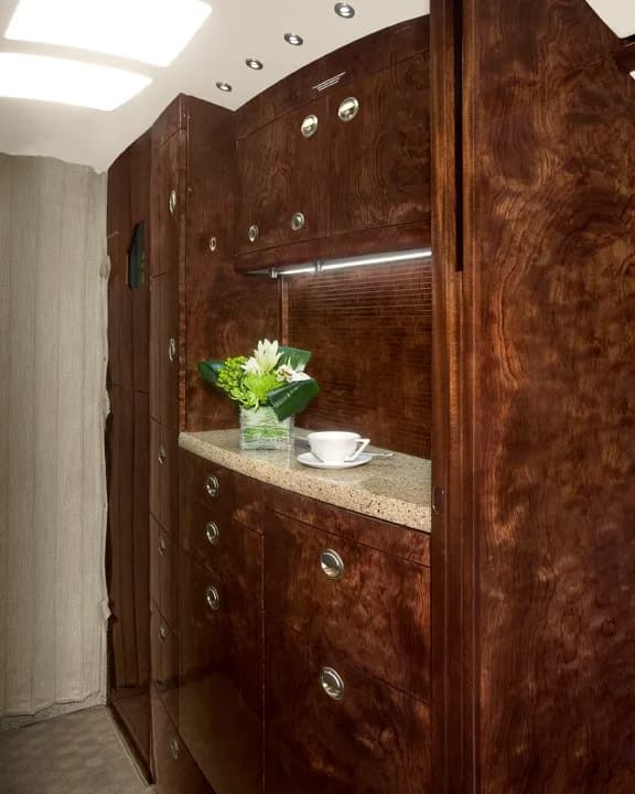 A detailed view of the dark wood cabinetry in a private jet's galley area, featuring a countertop with a small floral arrangement and a teacup.