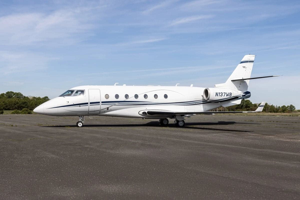 A white Gulfstream G150 aircraft with blue stripes, registration N137WB, is parked on the tarmac.