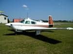 A white single-engine propeller aircraft with brown and orange accents parked on a grassy airfield.