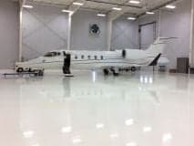 Learjet parked inside a hangar with a shiny floor and maintenance equipment.