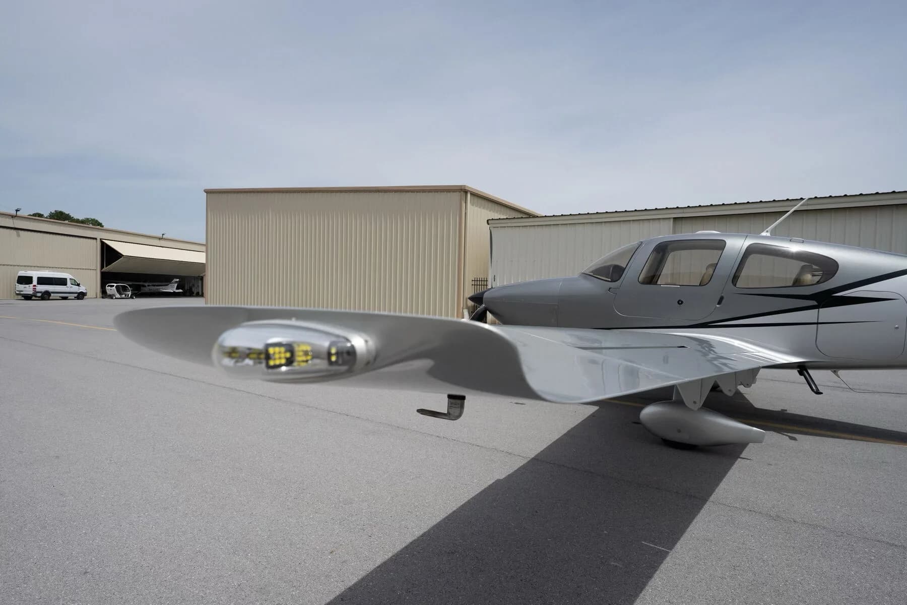 Close-up side view of the silver Cirrus SR22's fuselage and wingtip with landing lights.
