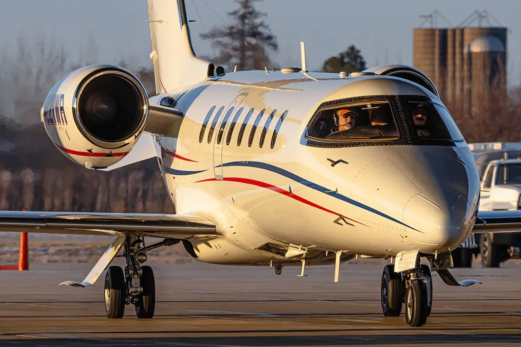 A close-up front view of a white Learjet 60, registration N221WP, with pilots visible in the cockpit, on the ground.