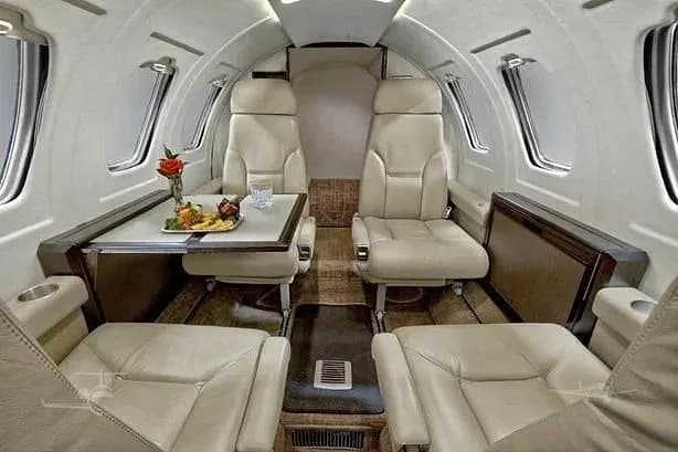 The luxurious interior cabin of a private jet features light-colored leather seats and a table set with food and drink.