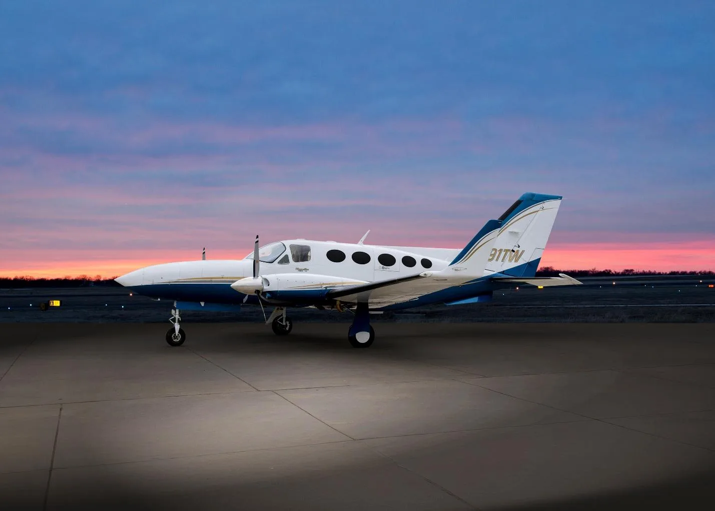 A white and blue Cessna 414 Chancellor (N91TW) parked on an airfield at sunset, viewed from the rear-right.