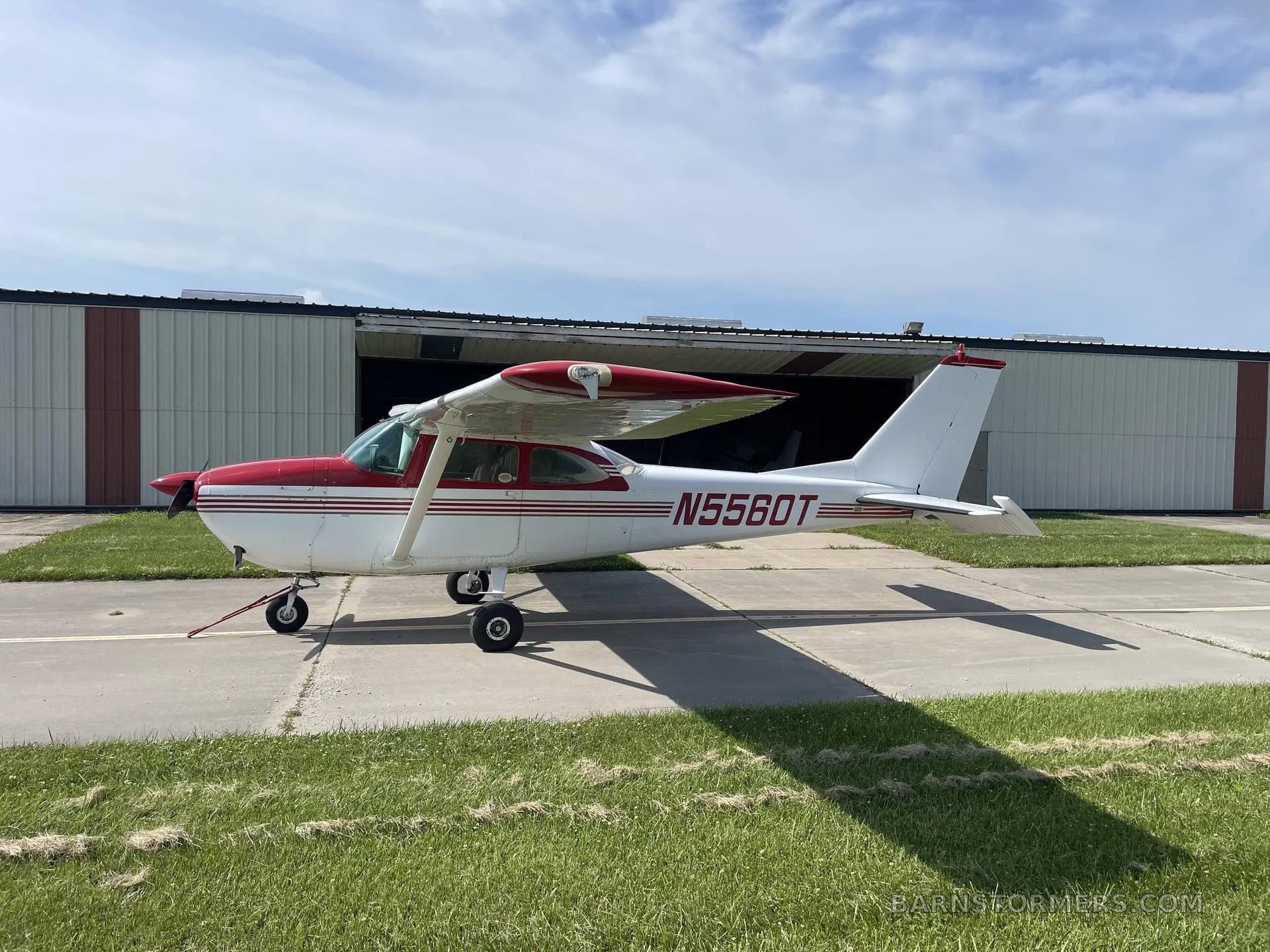 A white and red Cessna N5560T aircraft is parked on a concrete pad in front of an open hangar.