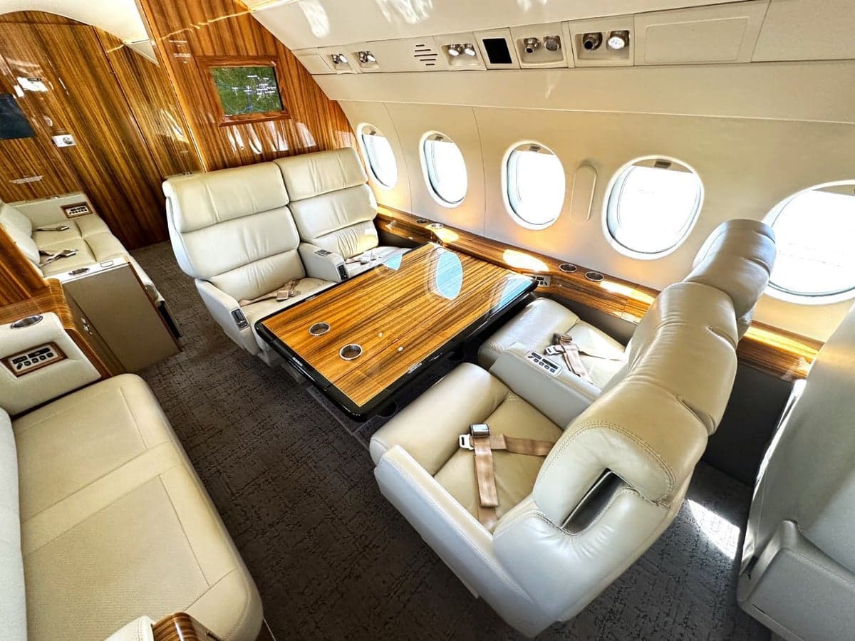 View of the aircraft's interior with cream-colored leather seats and a wooden table.