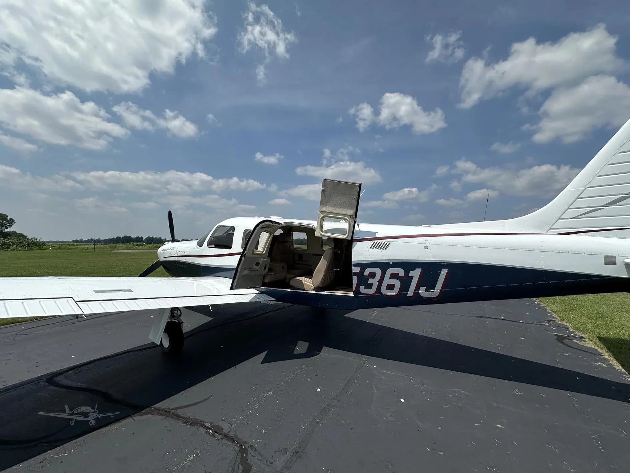 The white and blue Piper Saratoga II TC (N5361J) is parked with its cabin door open on an airfield.