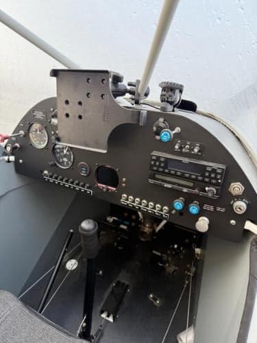 The cockpit of a Super Cub aircraft, showing the instrument panel with gauges, radios, and a control stick.