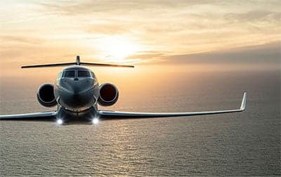A Gulfstream jet flying over the ocean at sunset.