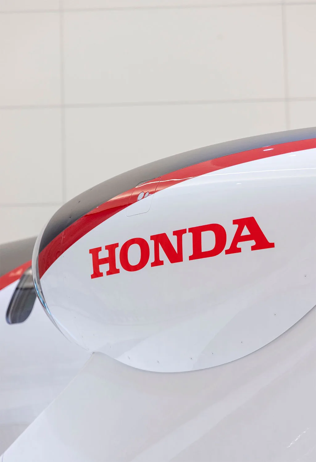A close-up view of the red 'HONDA' logo on the white engine nacelle of a HondaJet, with a red and black stripe.