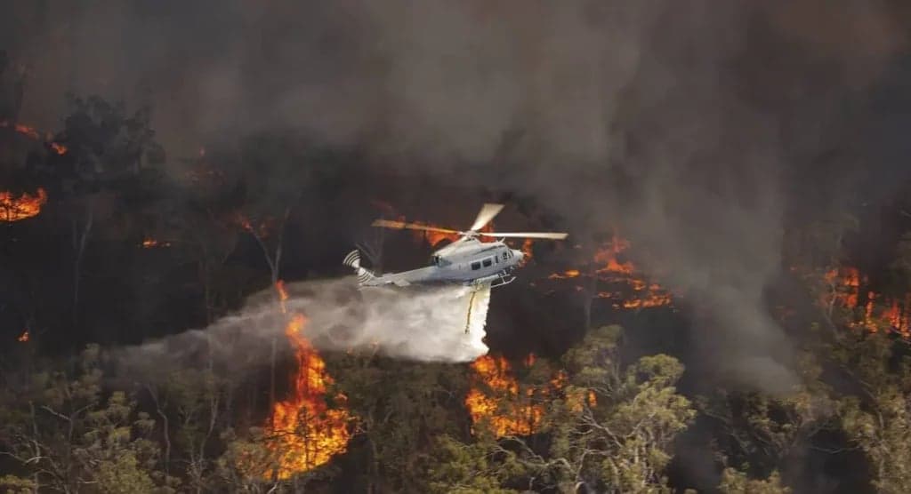 Bell UH-1 Iroquois helicopter dropping water on a forest fire.