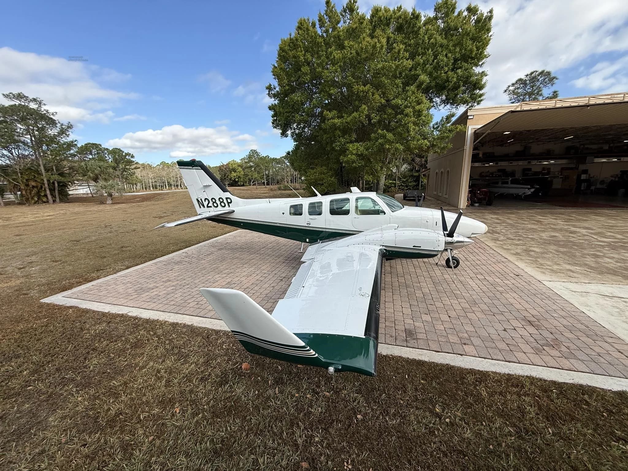 A white and green twin-engine Beechcraft Baron aircraft with tail number N288P parked outside a hangar.