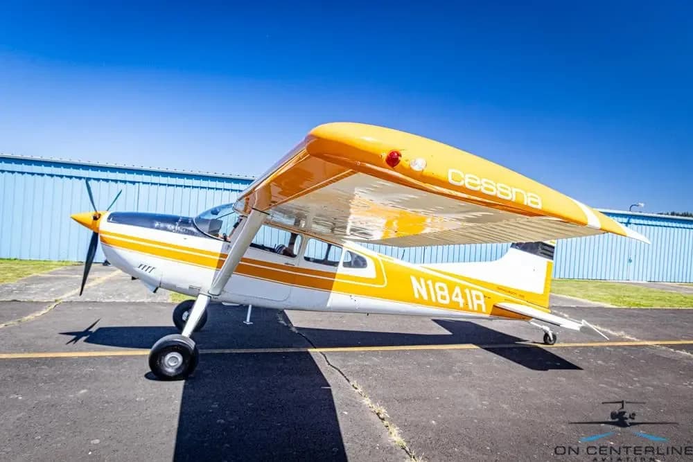 A front-side view of a white and orange Cessna 185 Skywagon (N1841R) with 'Cessna' on its orange wing.