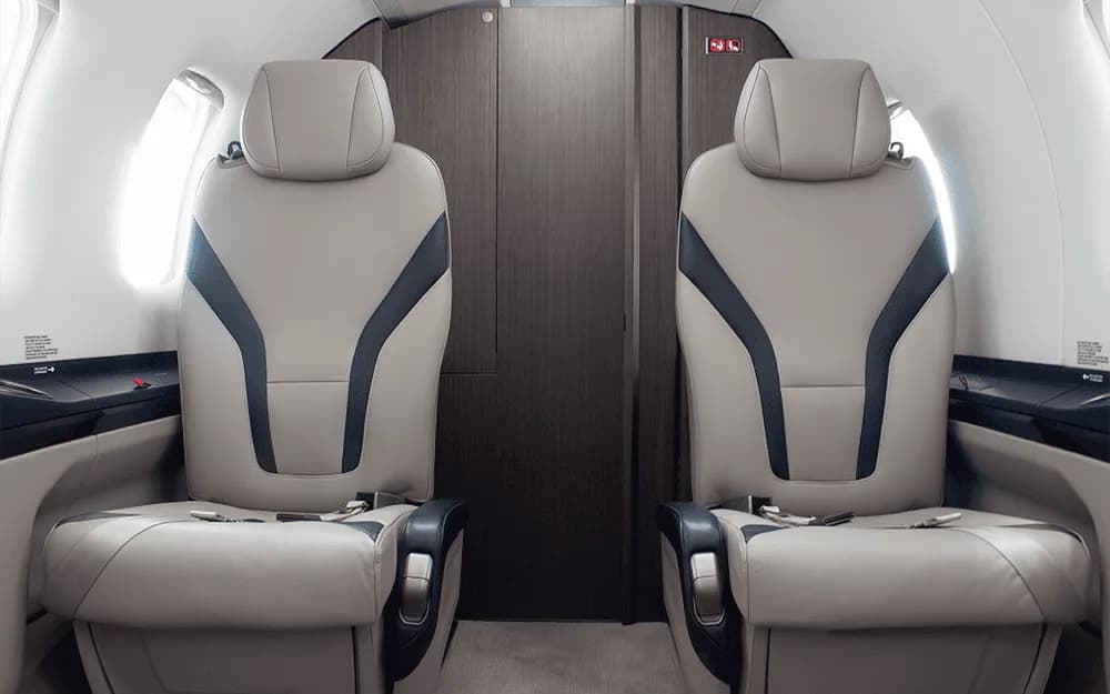 A close-up view of two light grey passenger seats with dark blue accents inside the Pilatus PC-12 cabin.