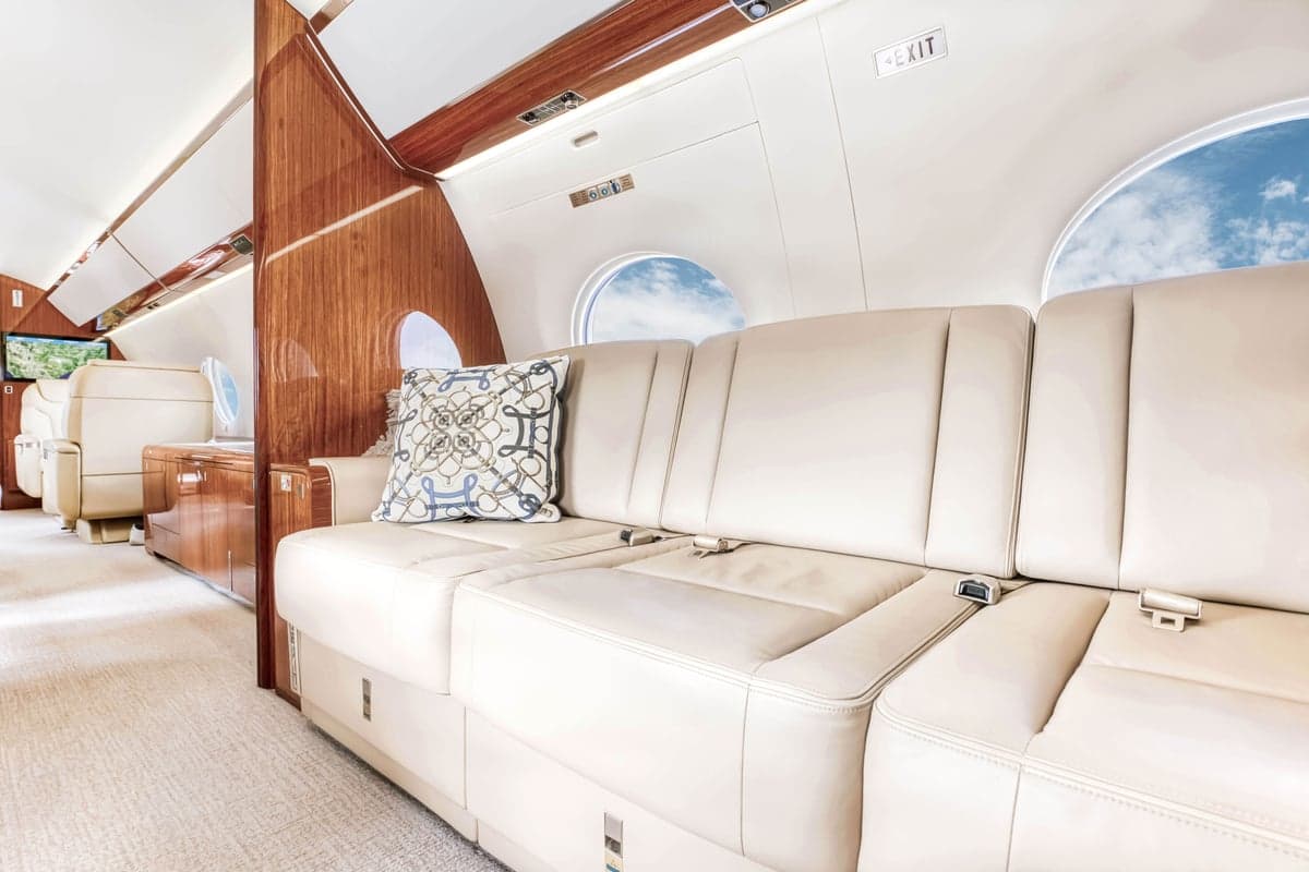 The aircraft's interior includes a cream-colored leather sofa and wood accents.