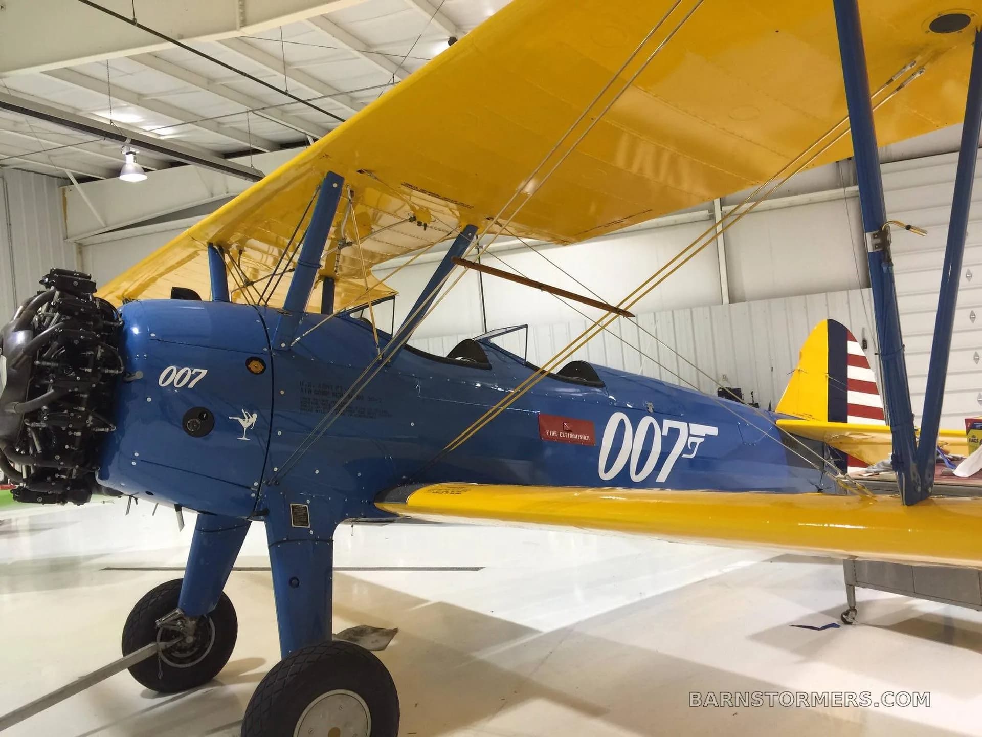 A blue and yellow biplane with "007" on its side is parked inside a brightly lit hangar.
