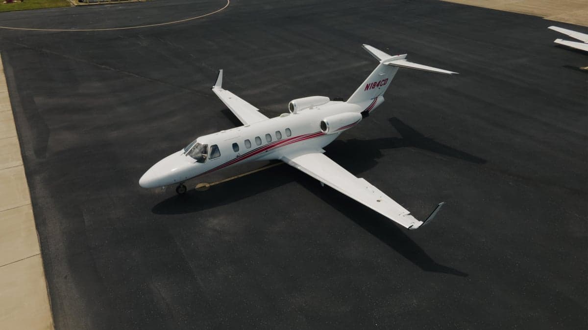 Aerial view of a white Citation CJ2 aircraft with red stripes parked on the tarmac.