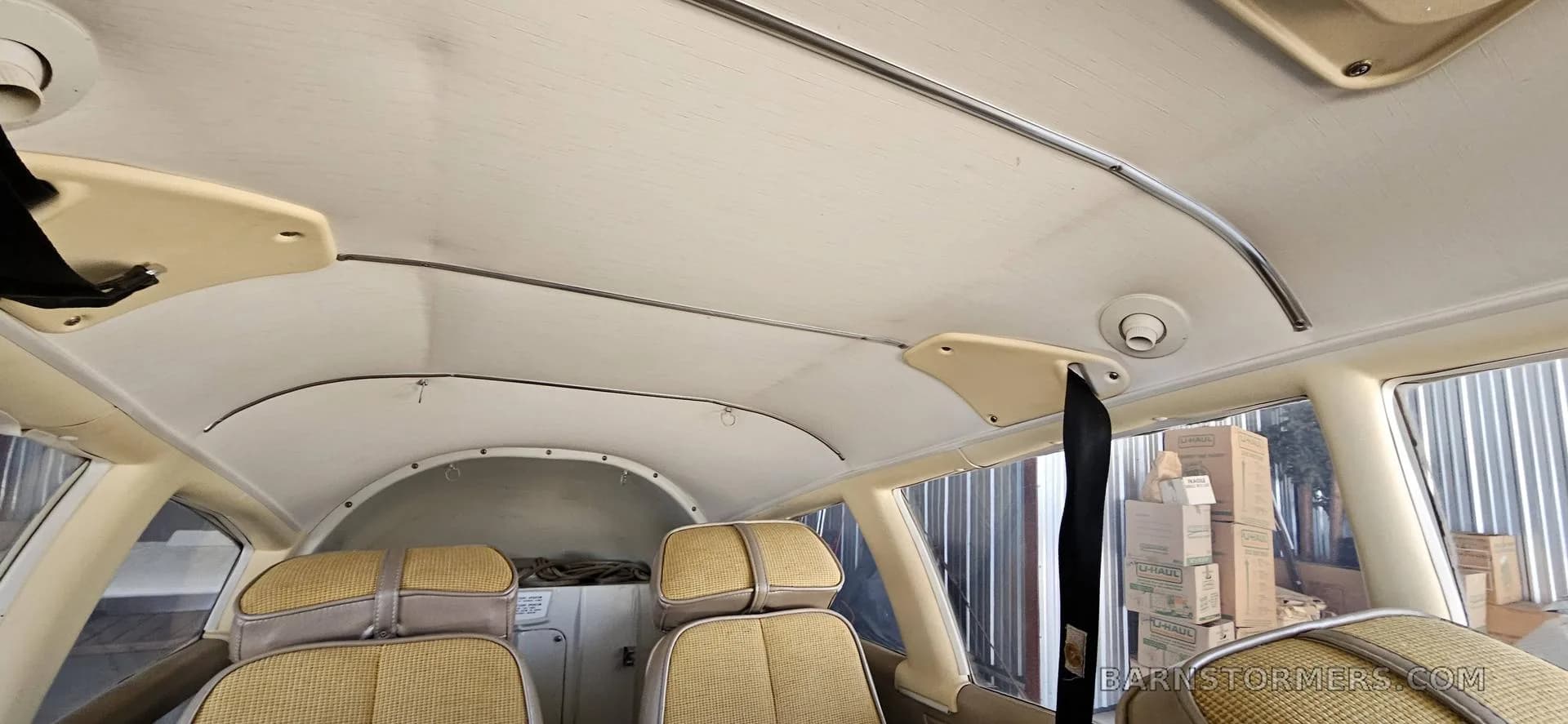 The tan ceiling and rear seats of a light aircraft cabin, with boxes visible outside the window.